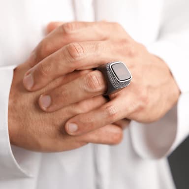 Hand wearing silver ring with square face on white robe background