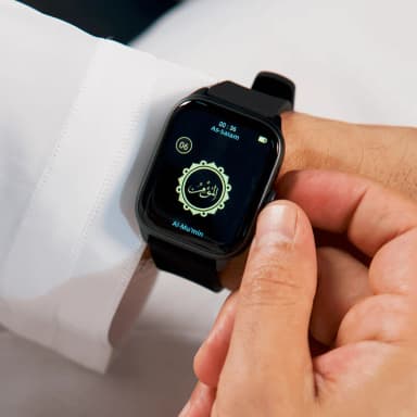 Hand wearing black smartwatch with Arabic clock face on white robe background