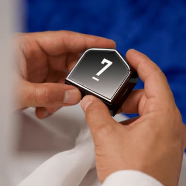 Hand holding black square device with number 7 on blue background